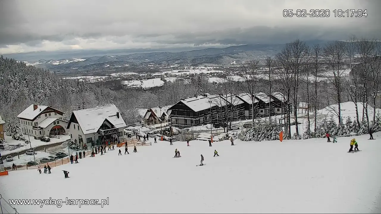 Widok z kamery na stok Karpatka pełen narciarzy, z panoramą Karpacza w tle